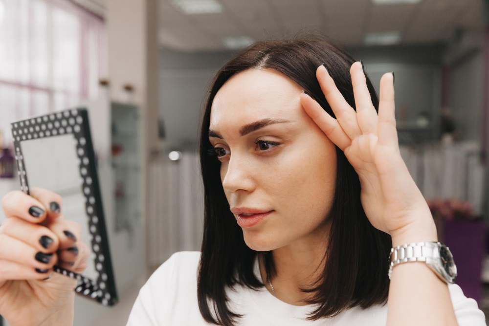 A woman looking at her eyebrows in the mirror after brow lift surgery