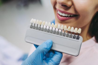 Dentist holding a tooth shade guide next to a patient’s smile for dental veneers