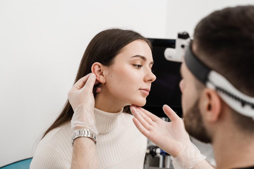Doctor with head mirror examining patient's ear for otoplasty surgery